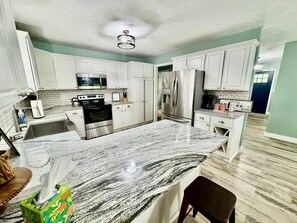 A modern kitchen with white cabinets, stainless steel appliances, and a marble countertop. - Stillwater Cottage at Norfork Lake (Mountain Home)