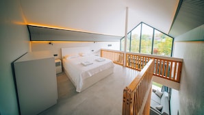 Quarto moderno com cama, mesa de cabeceira e vista para o verde através de grandes janelas.