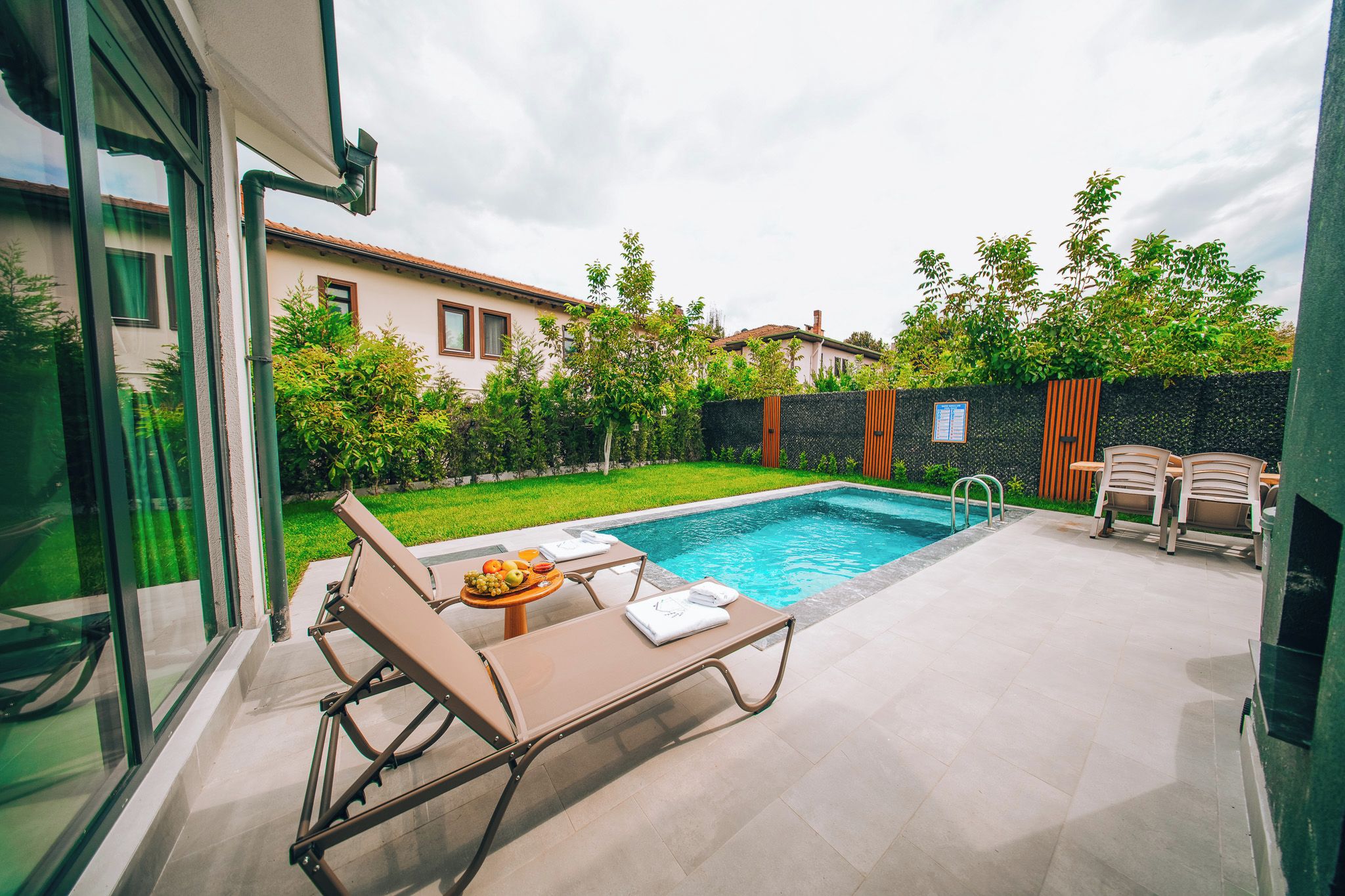 A modern outdoor pool area with lounge chairs and a table with fruit.