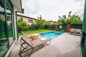 A modern outdoor pool area with lounge chairs and a table with fruit.