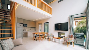 Uma sala de estar ampla com teto alto, mesa de jantar com cadeiras, sofá e televisão.