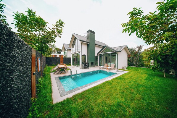 A modern house with a swimming pool, a covered patio, and a well-maintained lawn.