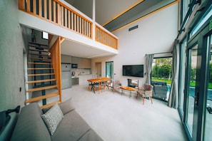 A modern interior with a dining area, sofa, staircase, kitchen, and a TV.