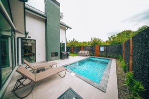 A modern outdoor pool area with lounge chairs, a barbecue grill, and a stone wall.