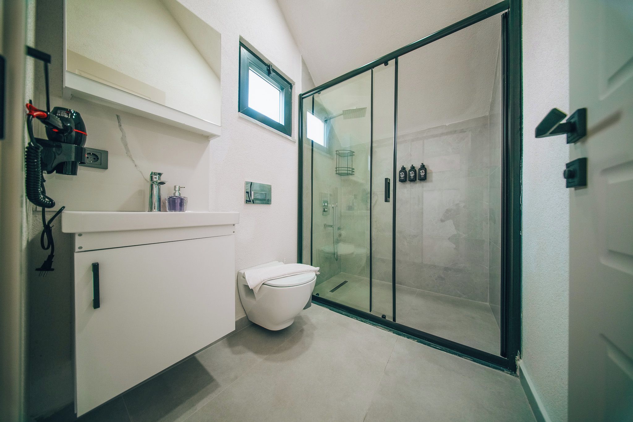 A modern bathroom with a toilet, a glass shower enclosure, and a vanity with a telephone and toiletries.