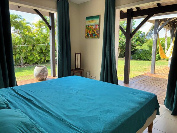 Una camera da letto con un letto grande, un quadro al muro e vista su un giardino attraverso tende aperte.