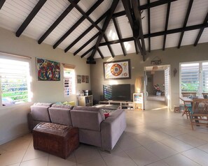 A spacious living room with a large sectional sofa, a flat-screen TV, and a dining area with wooden chairs. - Creole Villa in a Tropical Garden - 3 Bedrooms & 2 Bathrooms (Sainte-Anne)