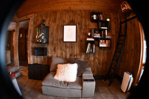 A cozy room with a wooden interior, a sofa with a fluffy pillow, a bookshelf, and a ladder. - 5BR All-Sports Lakehouse · Hot Tub + Pontoon · Portage (Portage)