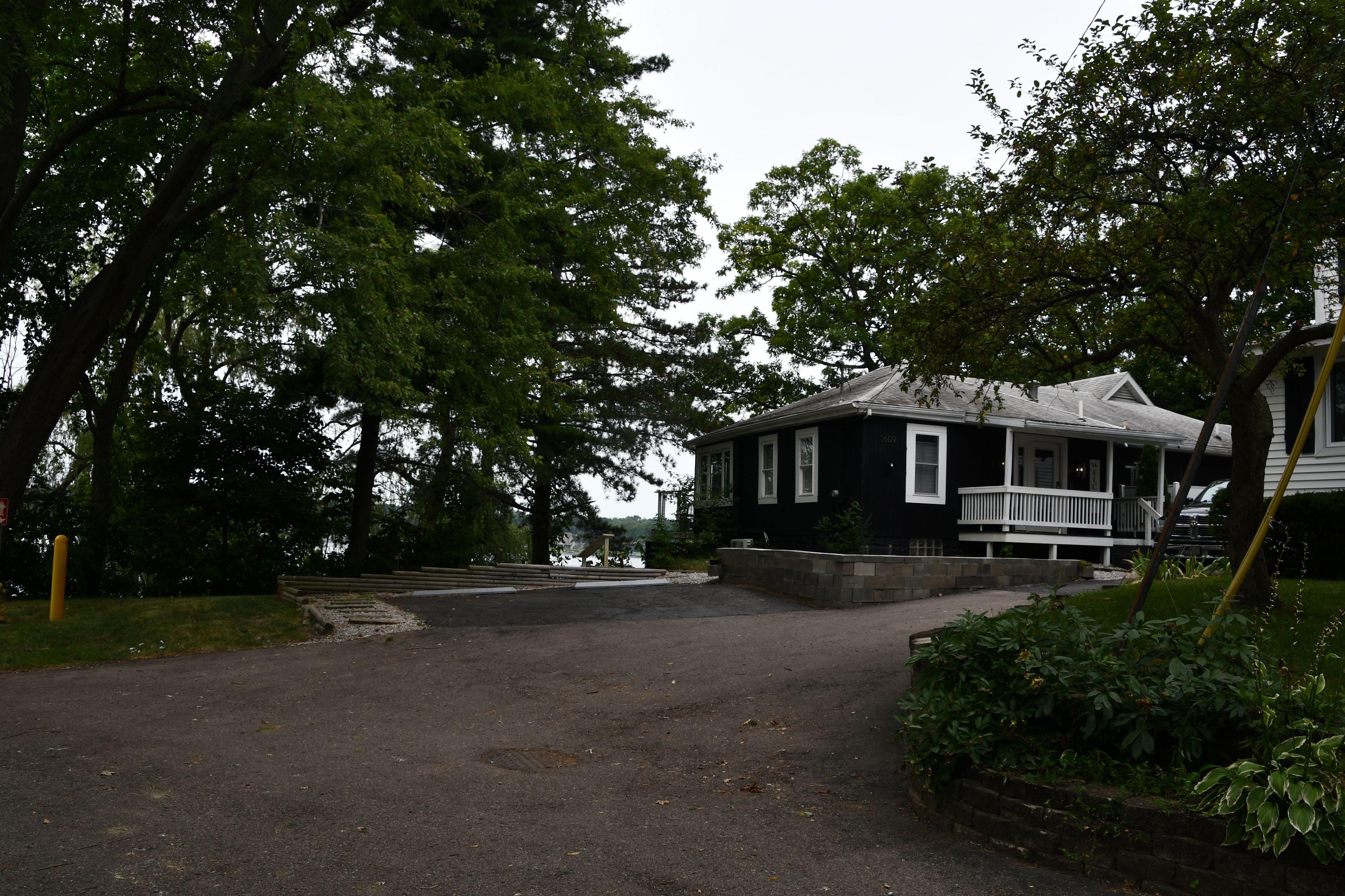 A two-story house with a porch and a driveway leading to a dock.