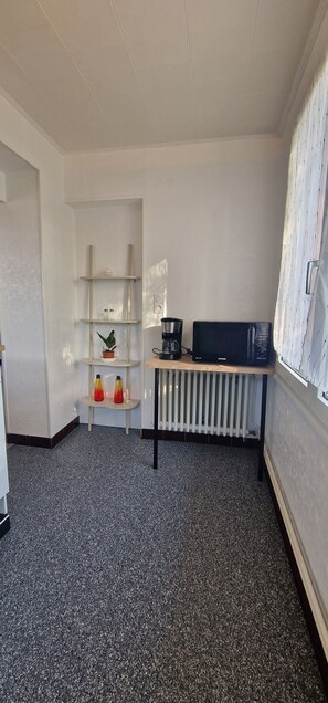 A room with a radiator, a shelf with decorative items, and a television on a wooden table.
