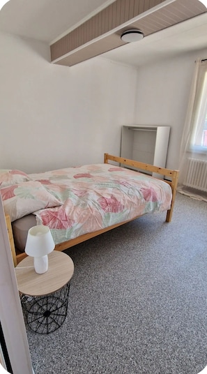 Ein Einzelbett mit floraler Bettdecke in einem Zimmer mit schrägen Wänden und einer Heizung.