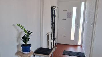 A hallway with a potted plant, a small stool, a metal rack, and a door leading to another room.
