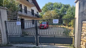Une propriété privée, fermée par un portail, où se trouve une voiture rouge garée à l’intérieur, ainsi qu’un balcon et une enseigne indiquant la présence d’un restaurant.