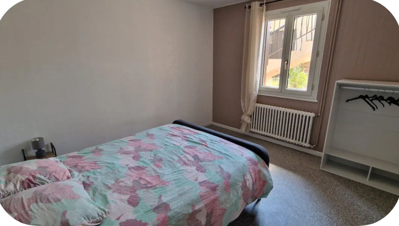 Une chambre à coucher avec un lit, un radiateur et une fenêtre avec des rideaux.