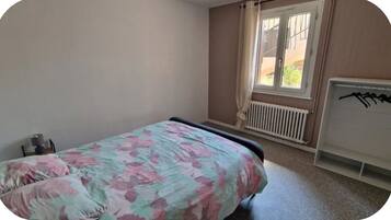 Une chambre à coucher avec un lit, un radiateur et une fenêtre avec des rideaux.