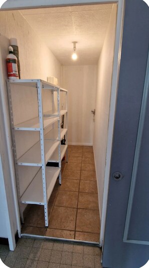 A narrow hallway with a metal shelving unit against the wall, a tiled floor, and a door at the end.