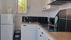 Una cocina con armarios blancos, encimera negra y ventana con vistas a árboles.