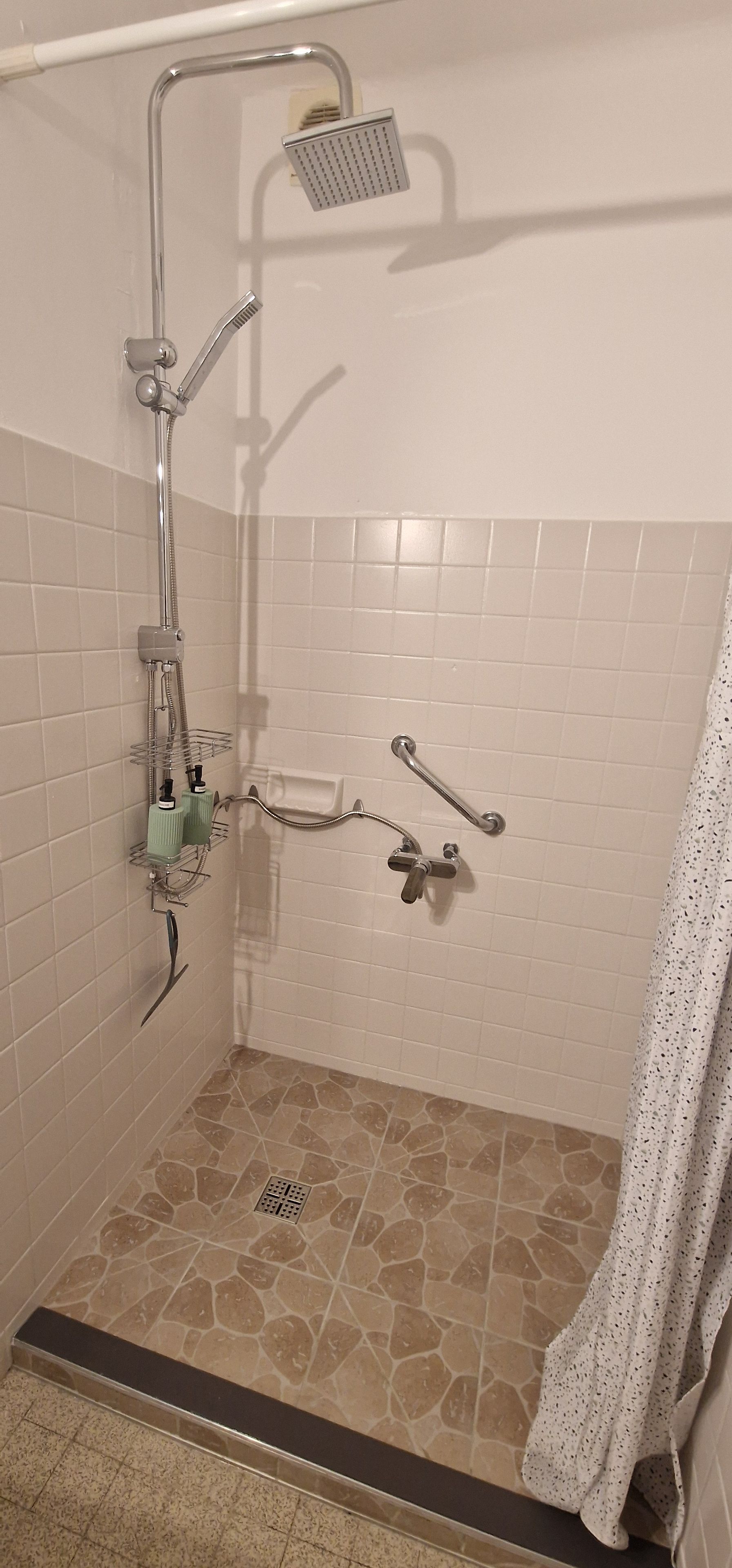 Une douche équipée d’un pommeau de douche à main, d’un robinet mural et d’un pommeau de douche à main.