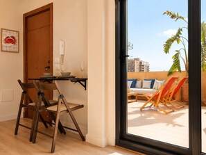 A room with a wooden dining table, two chairs, a door, and a view of a balcony with chairs and a plant. - Solé Mare Rooftop Studio I Nesty Hospitality (Al Maadi)