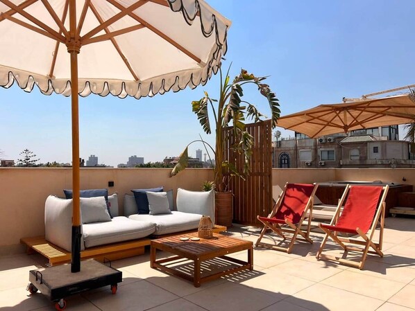 A rooftop terrace with a sofa, chairs, a table, and an umbrella. - Solé Mare Rooftop Studio I Nesty Hospitality (Al Maadi)