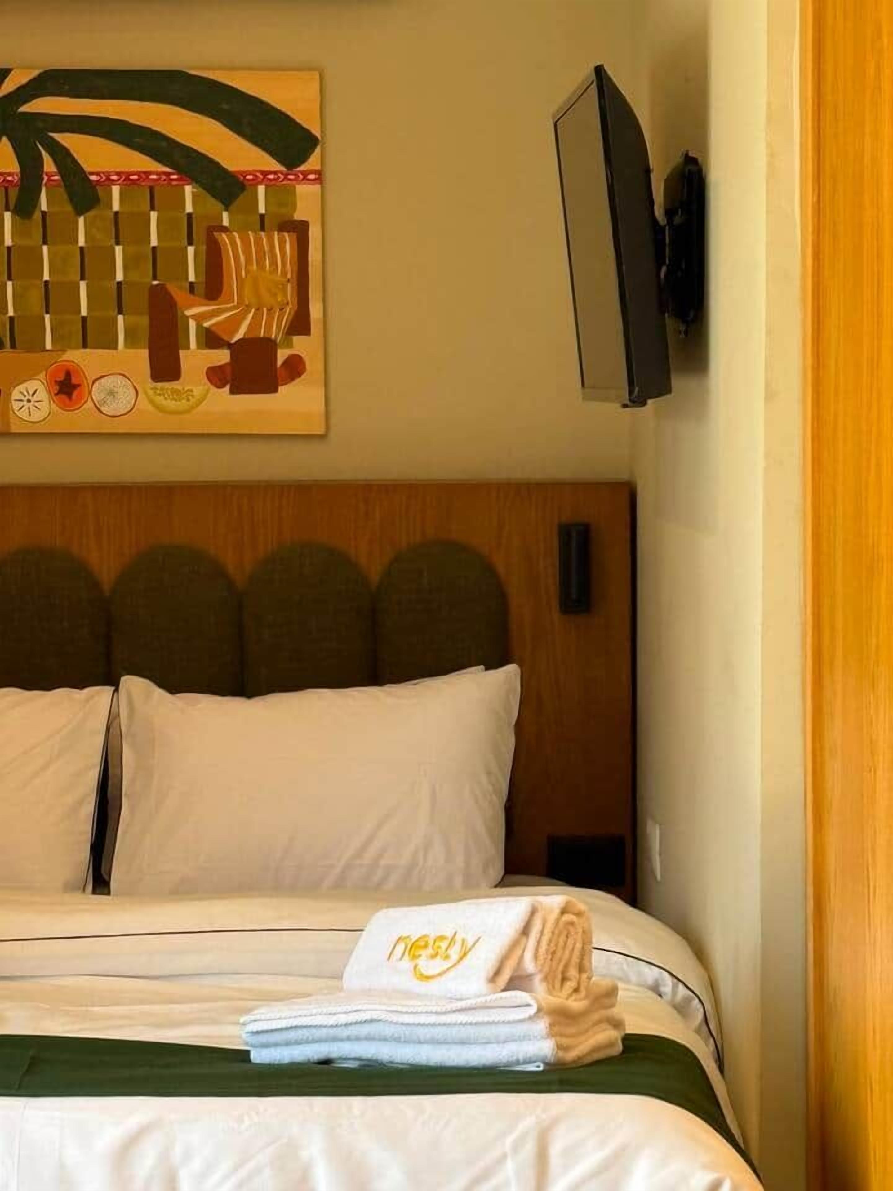Hotellihuone, jossa on sänky, seinälle asennettu televisio ja taulu.