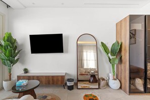 A modern living room with a flat-screen TV, a wooden bench, a round coffee table, and two large potted plants. - Maraya Hideaway Private Jacuzzi| Nesty Hospitality (Second Hurghada)