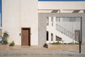 Une façade moderne avec une porte en bois, un escalier doté de rampes en métal et un jardinier avec des plantes.