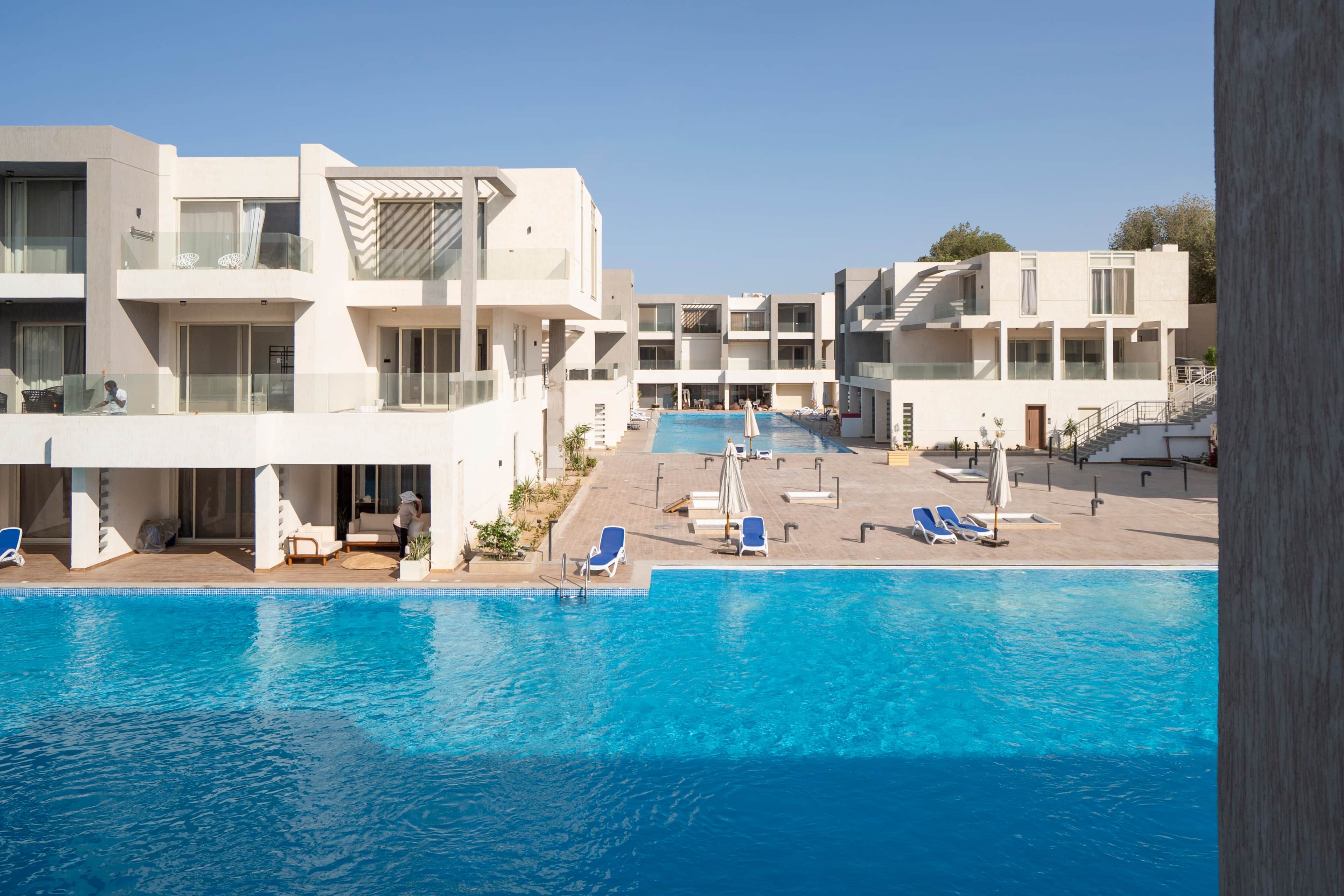 Um hotel moderno com piscina, várias varandas e espreguiçadeiras.