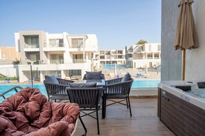 A poolside area with lounge chairs, a hot tub, and a view of modern buildings. - Maraya Hideaway Private Jacuzzi| Nesty Hospitality (Second Hurghada)
