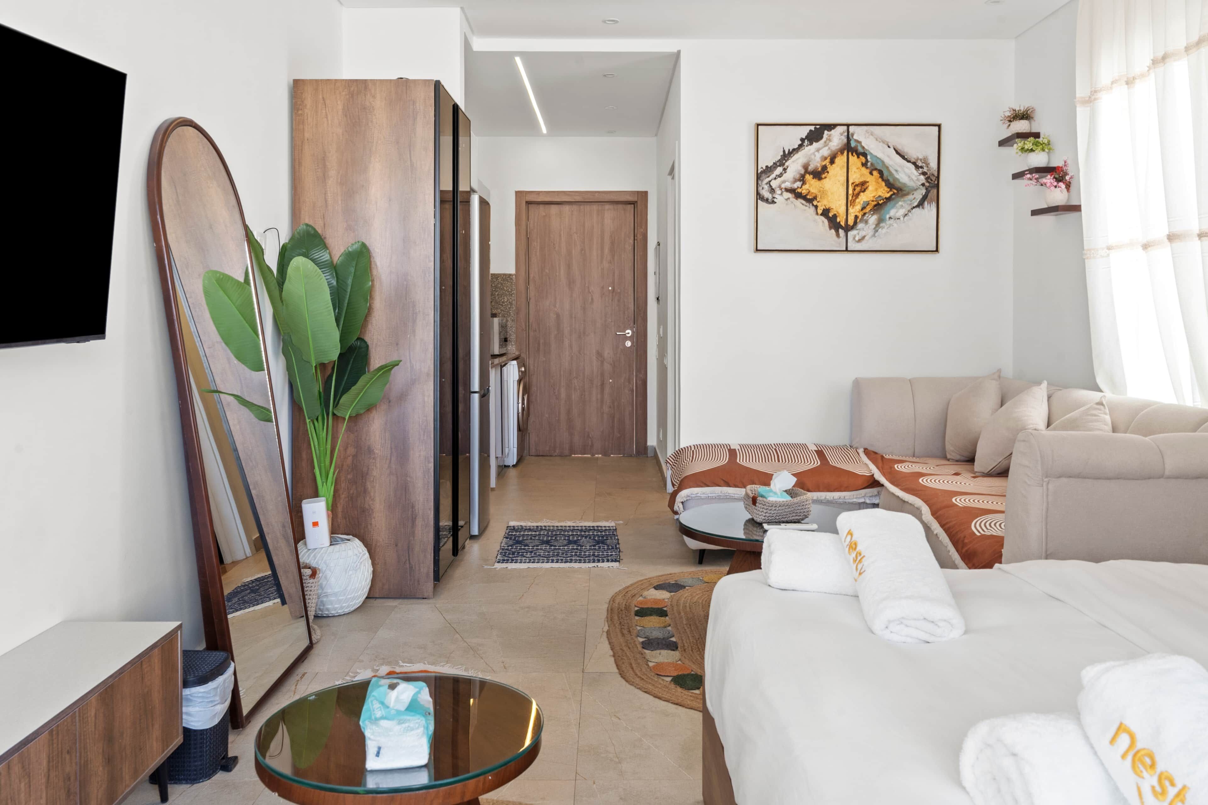 Une chambre d’hôtel moderne avec un lit, un canapé, une table basse en verre, un grand miroir et un tableau au mur.