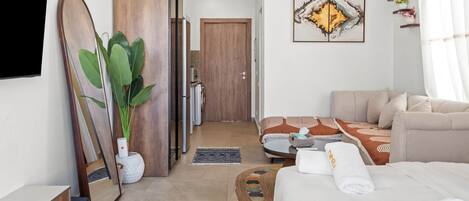 A modern hotel room with a bed, a sofa, a glass coffee table, a large mirror, and a painting on the wall.