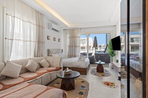 A hotel room with a sofa, a bed, a small table, and a view of the city. - Maraya Hideaway Private Jacuzzi| Nesty Hospitality (Second Hurghada)