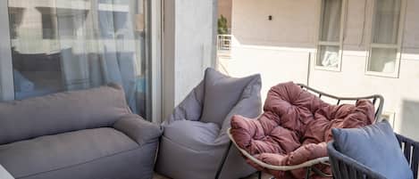 A balcony with a grey sofa, a cushioned chair, and a small table with a remote control.