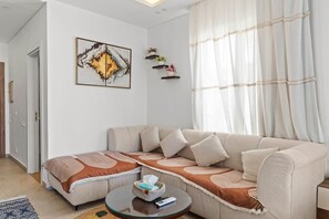 Un salon avec un canapé beige, une table basse en verre et un tableau accroché au mur.
