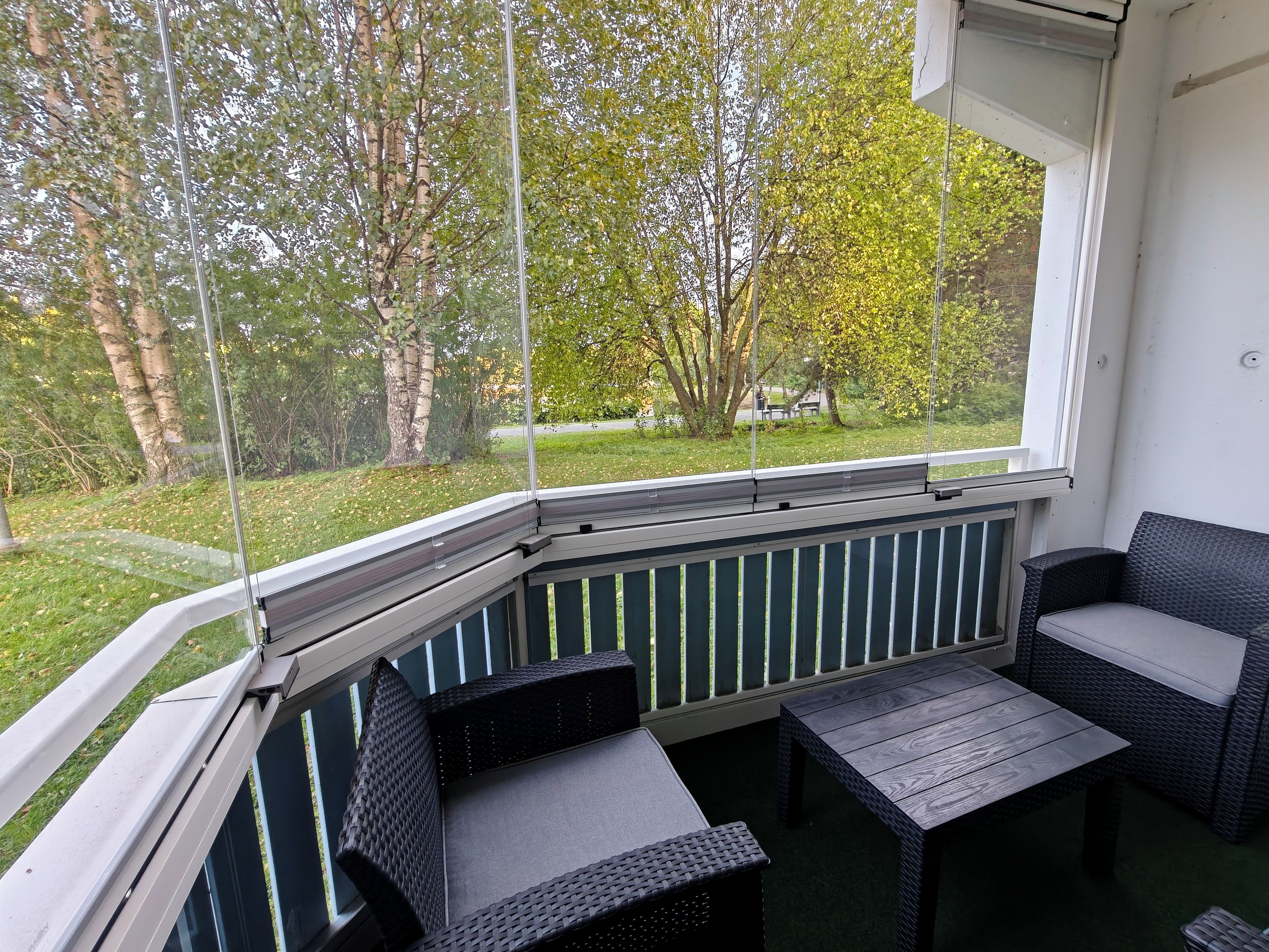 Katettu ulkoalue, jossa on istumapaikkoja ja josta avautuu näkymä vehreään puistoon ja puihin.