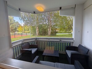 Ein Eckbalkon mit Korbmöbeln, Blick auf einen Park und einer Deckenleuchte.