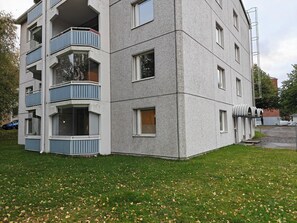 Ein mehrstöckiges Gebäude mit Balkonen, einer flachen Dachterrasse und einer Rasenfläche davor.