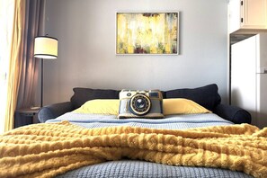 A hotel room with a bed, a lamp, a camera, and a painting on the wall. - Steps to Beach-Ocean View-1bd1ba- Sleeps 5-Pool (Galveston)