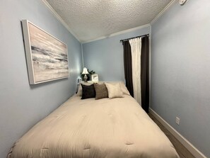 Ein Schlafzimmer mit einem Bett, einem Nachttisch, einer Lampe und einem Bild an der Wand.