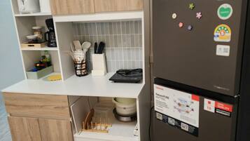 A compact kitchen with wooden cabinets, a white countertop, a refrigerator with magnets, and a small clock on the wall.