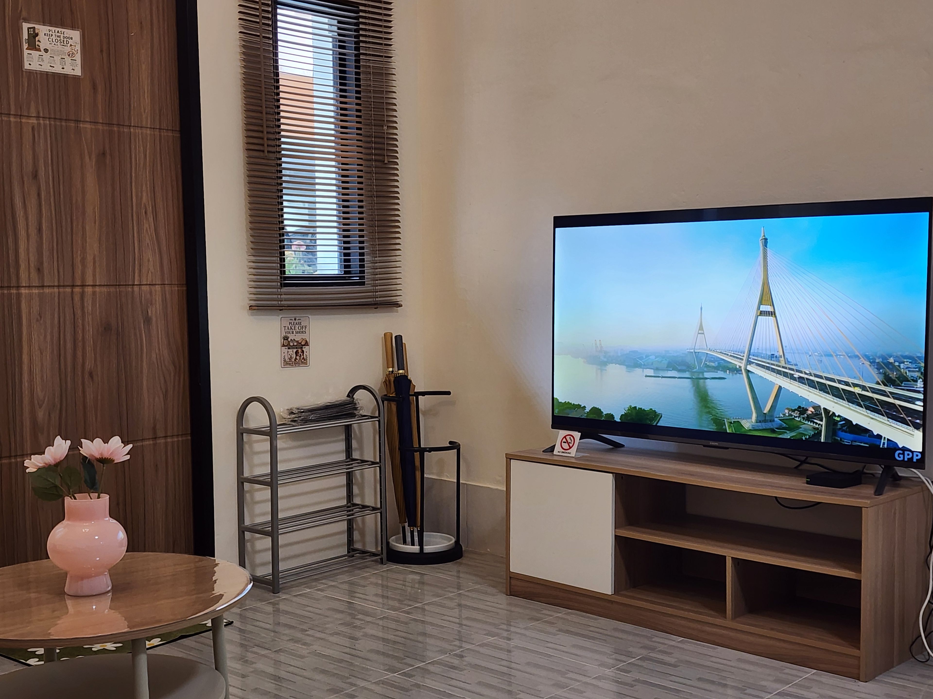 A room with a television displaying a bridge, a wooden cabinet, a metal shelf unit, and a small table with a vase.