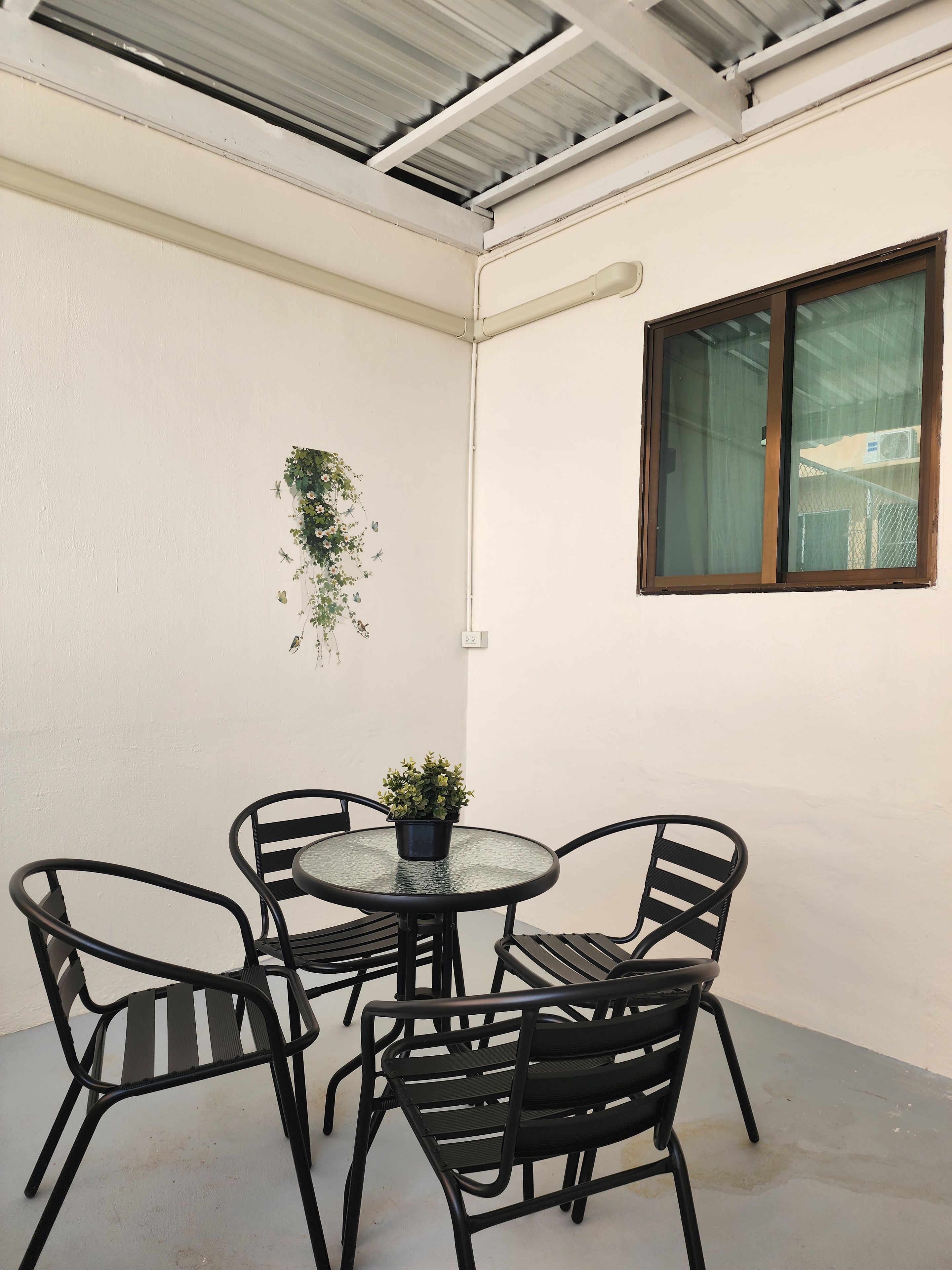 A corner of a room with a round table and four chairs, a window, and a wall-mounted plant.
