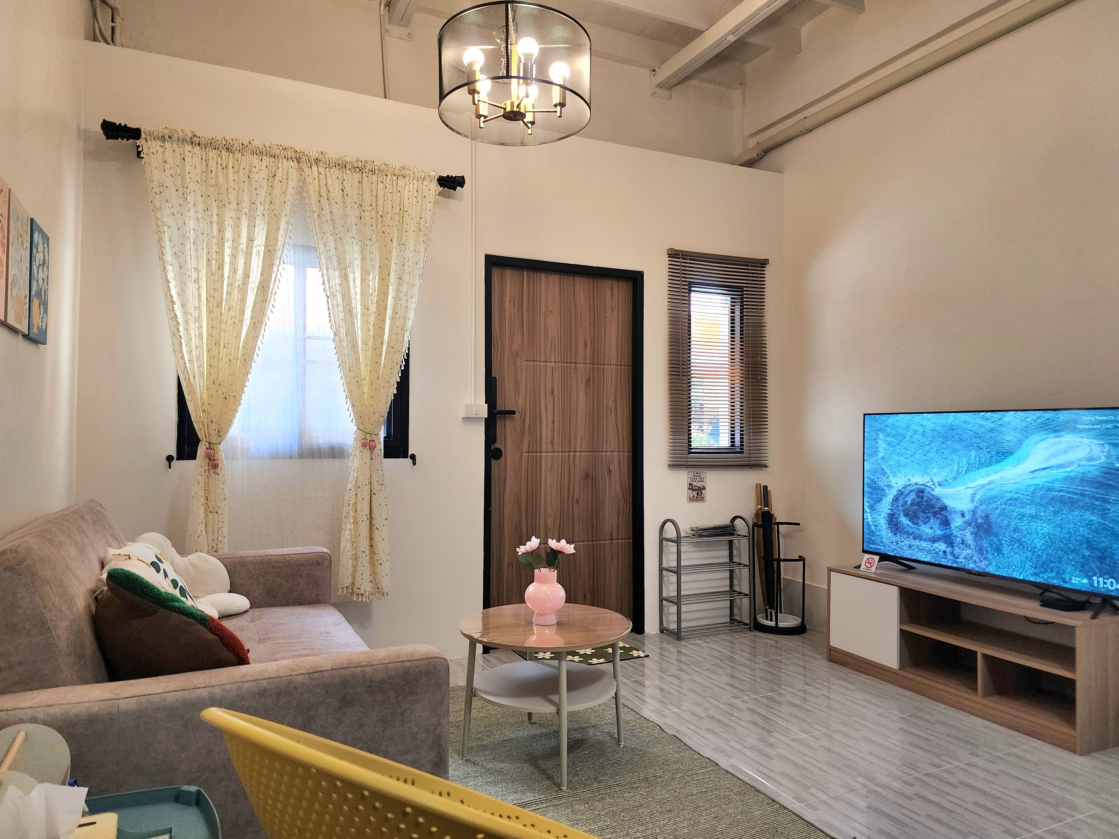 A living room with a sofa, a television, a small table with a pink vase, and a door.