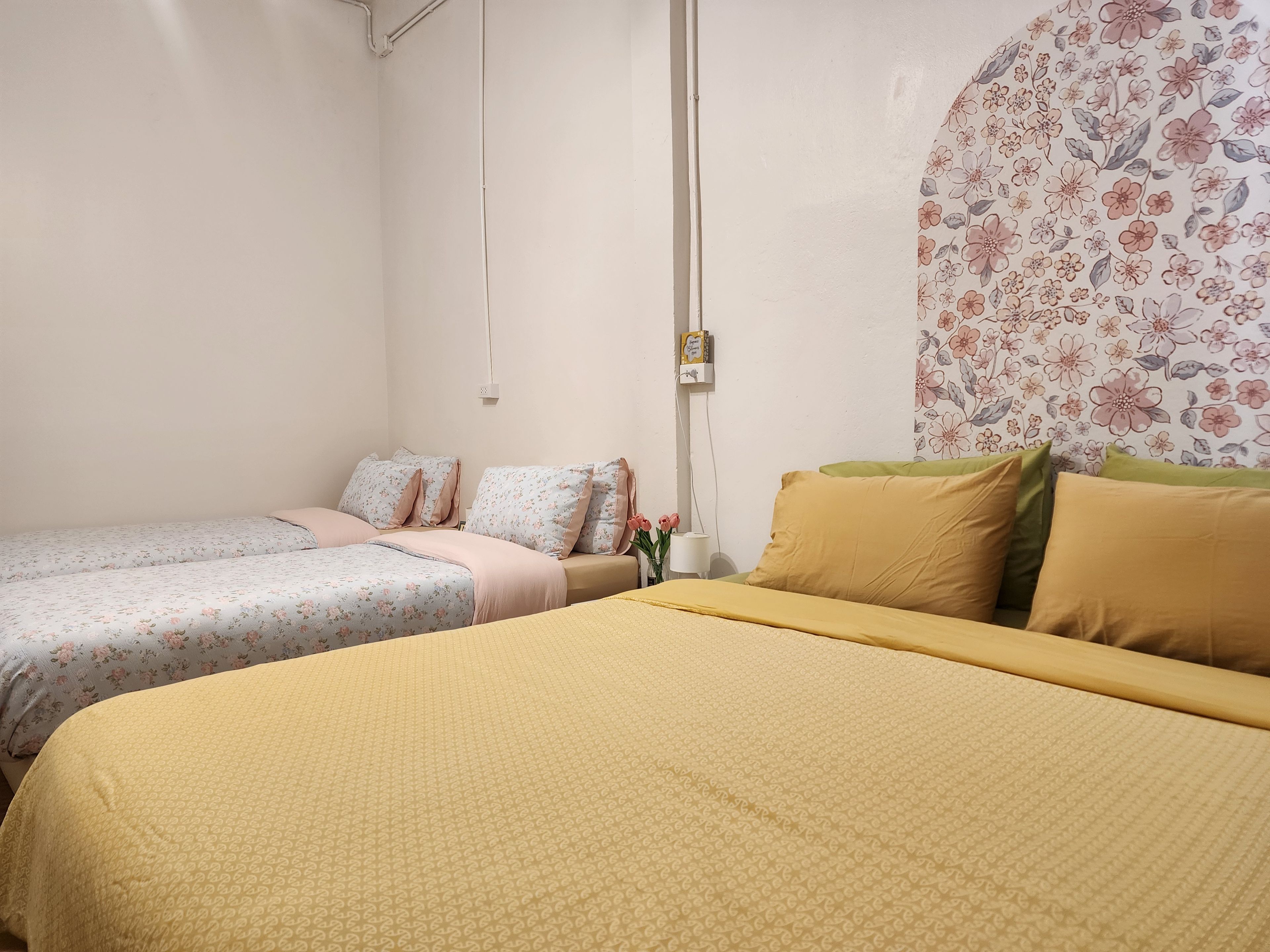 A room with two single beds, one with a floral-patterned bedspread and the other with a solid yellow bedspread.