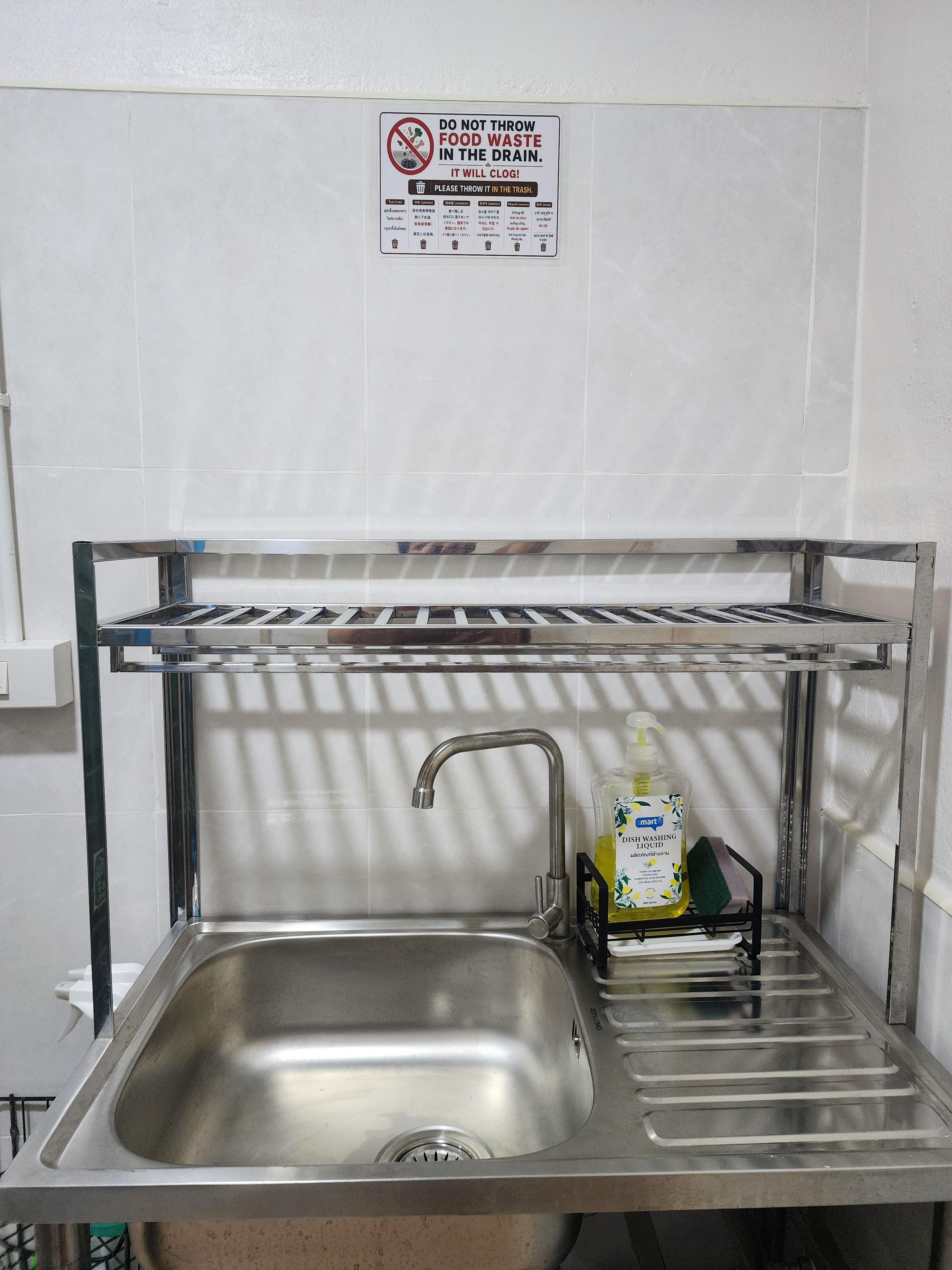 A stainless steel kitchen sink with a faucet, a shelf above it, and a bottle of dishwashing liquid.