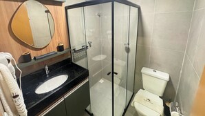 Un baño moderno con ducha envuelta en vidrio, un espejo redondo y un lavamanos con encimera negra.