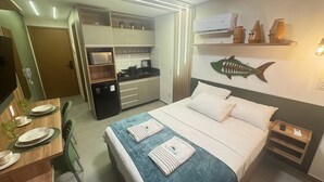 Habitación de hotel con cama, escritorio con silla, minibar, microondas y aire acondicionado de pared.