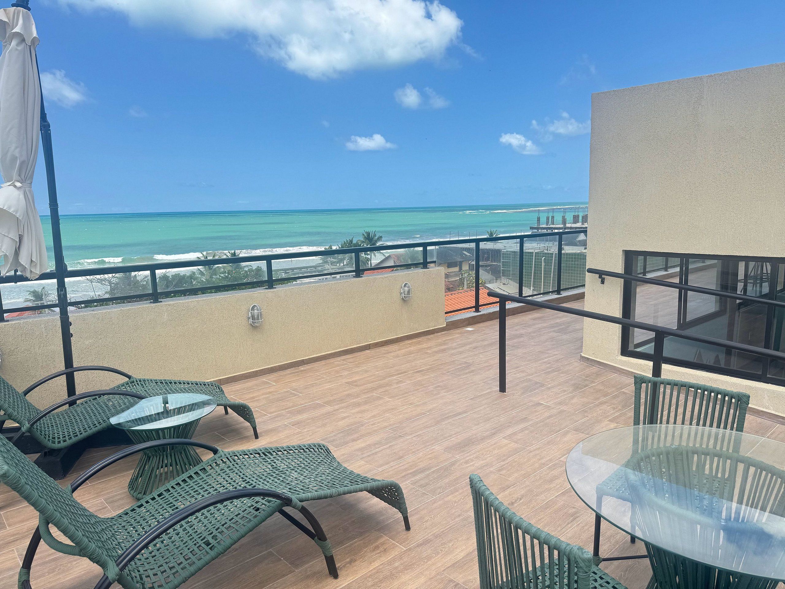 Varanda com vista para o oceano, equipada com cadeiras de vime e uma mesa de vidro.