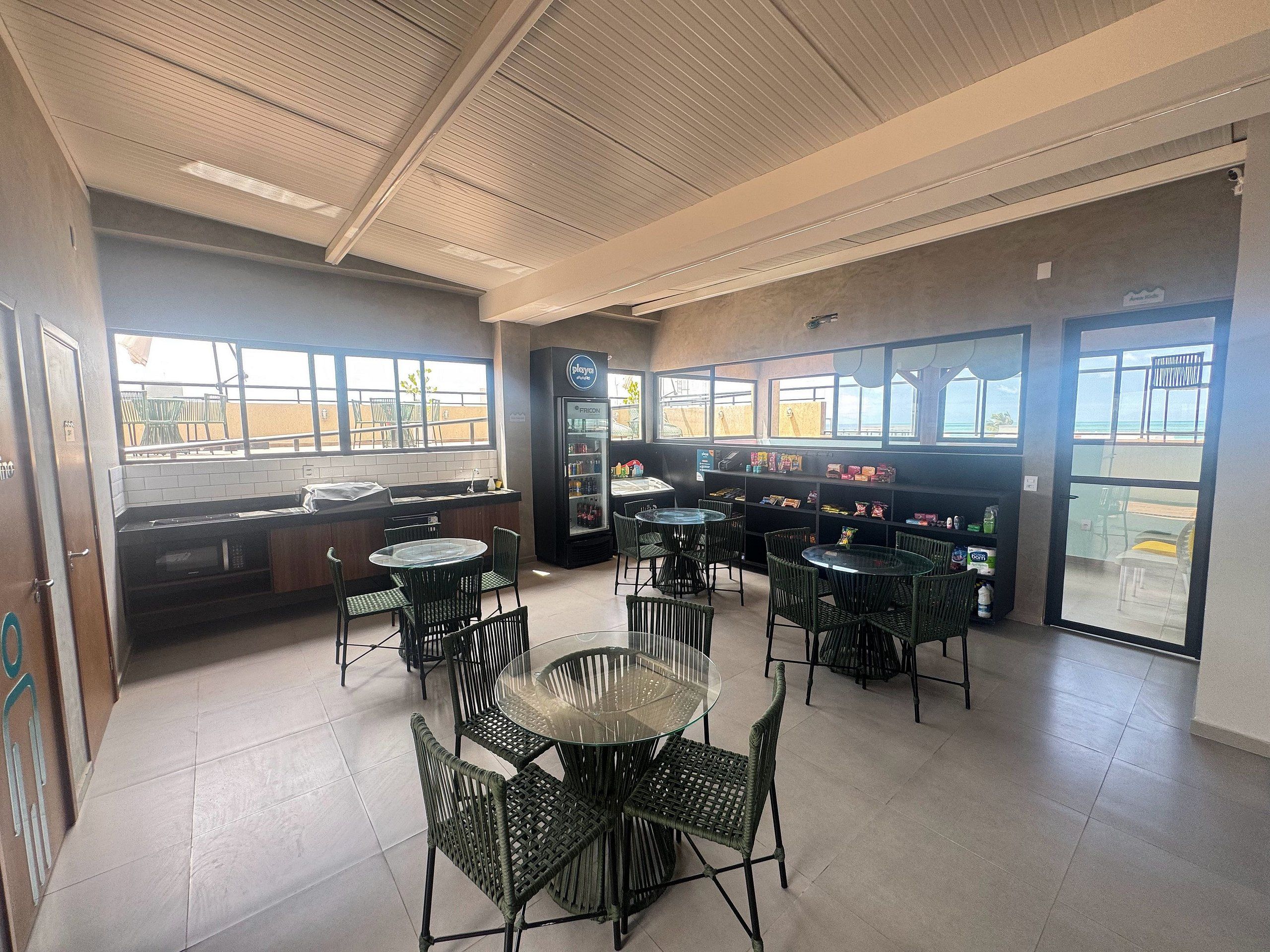 L’intérieur d’un restaurant, avec de nombreuses tables et chaises, un réfrigérateur et une vue sur l’extérieur par les fenêtres.