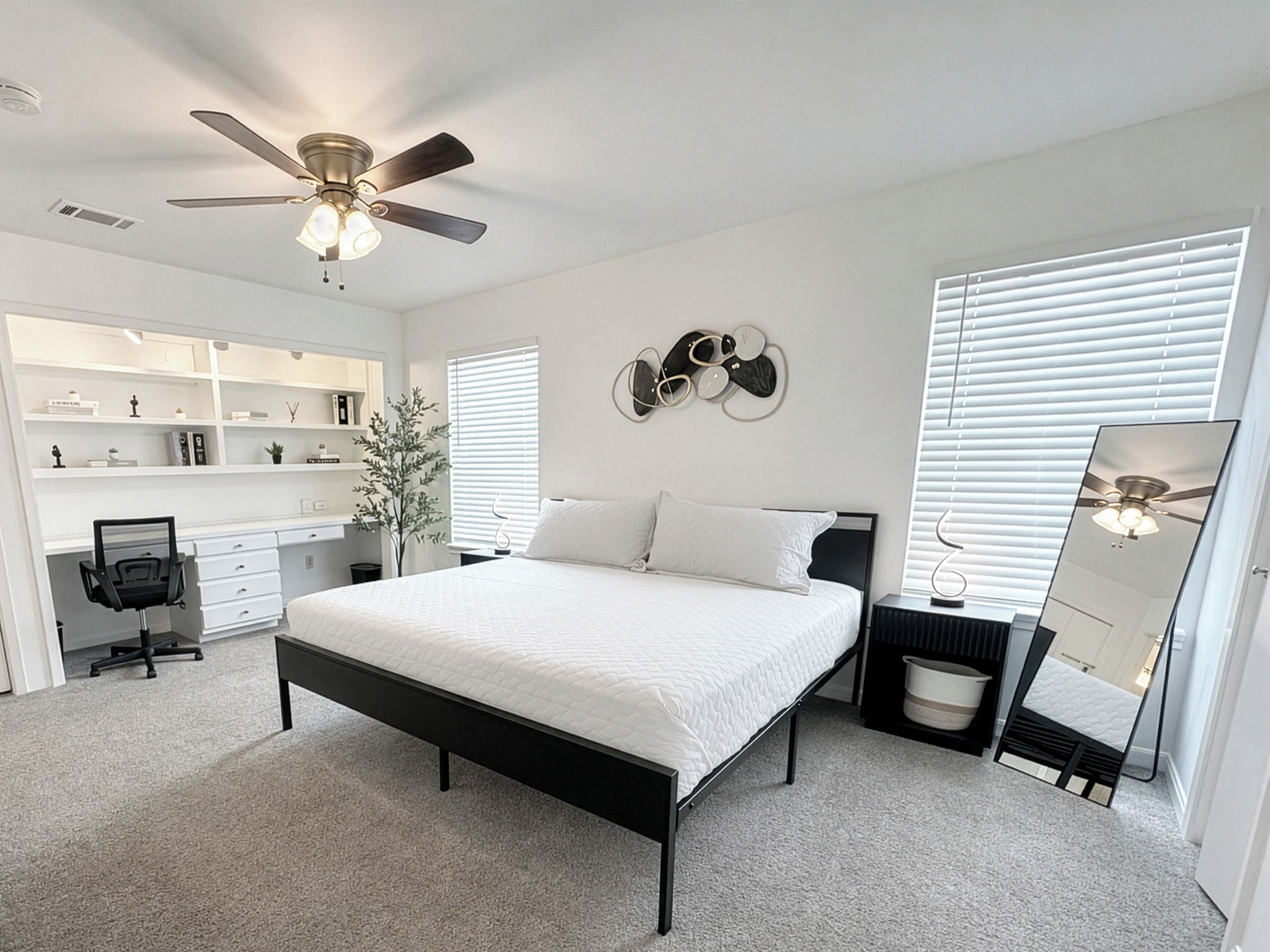 A bedroom with a bed, a desk, a chair, a wardrobe, a ceiling fan, and a wall-mounted mirror.